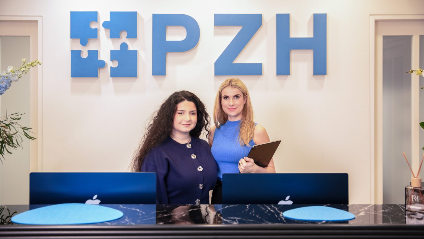 Zwei Mitarbeiterinnen des PZH am Empfangstresen vor der Wand mit dem PZH-Logo